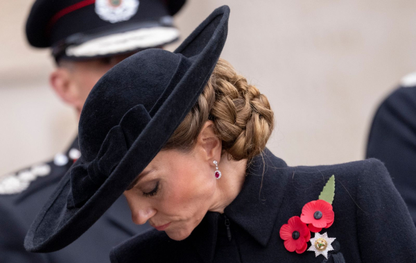Kate Middleton wears a knotted twisted side bun under a black hat.